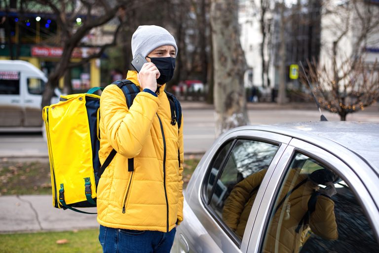 courier with yellow backpack black medical mask near car talking phone 768x513
